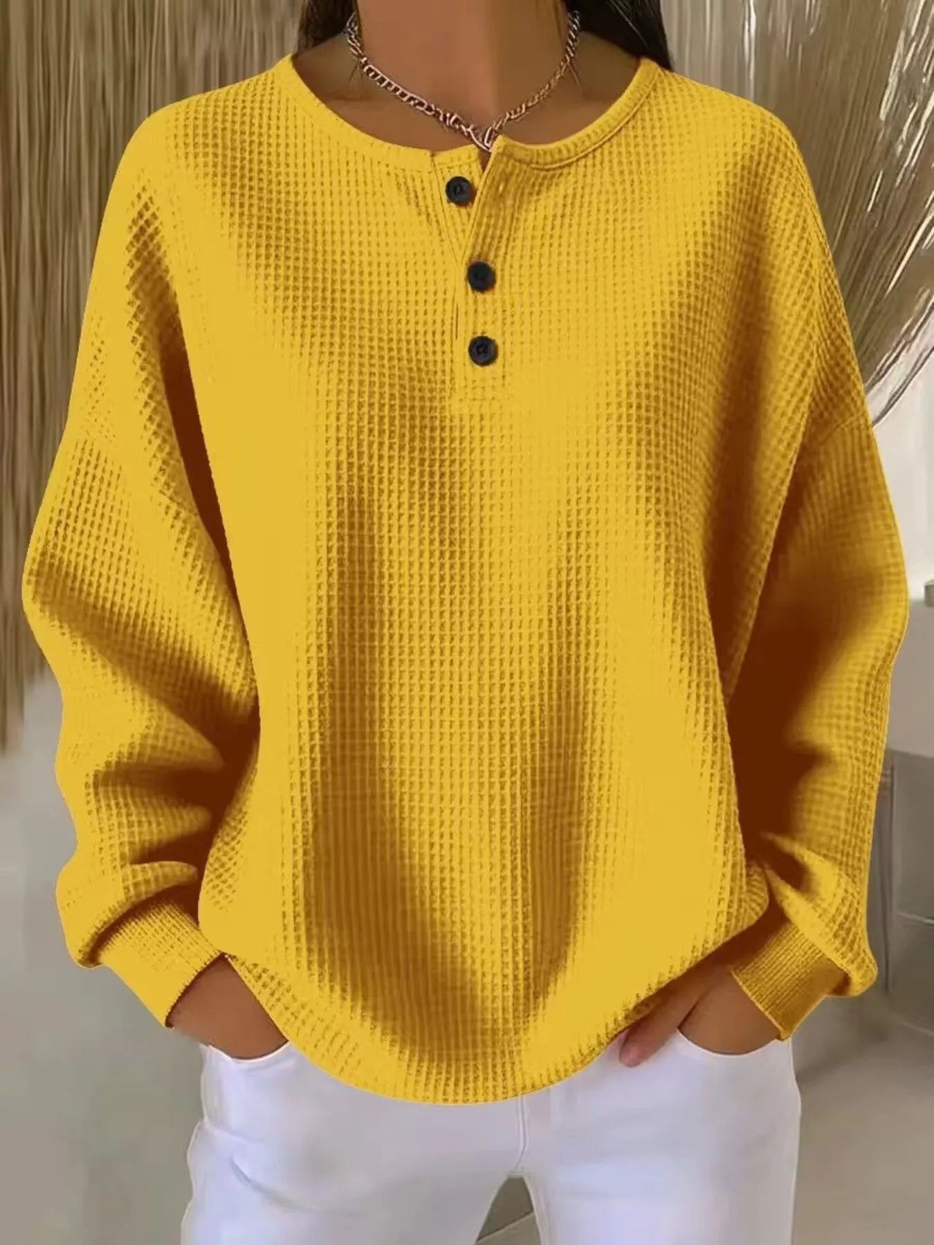Yellow textured sweater with black buttons worn by a person, against a neutral background