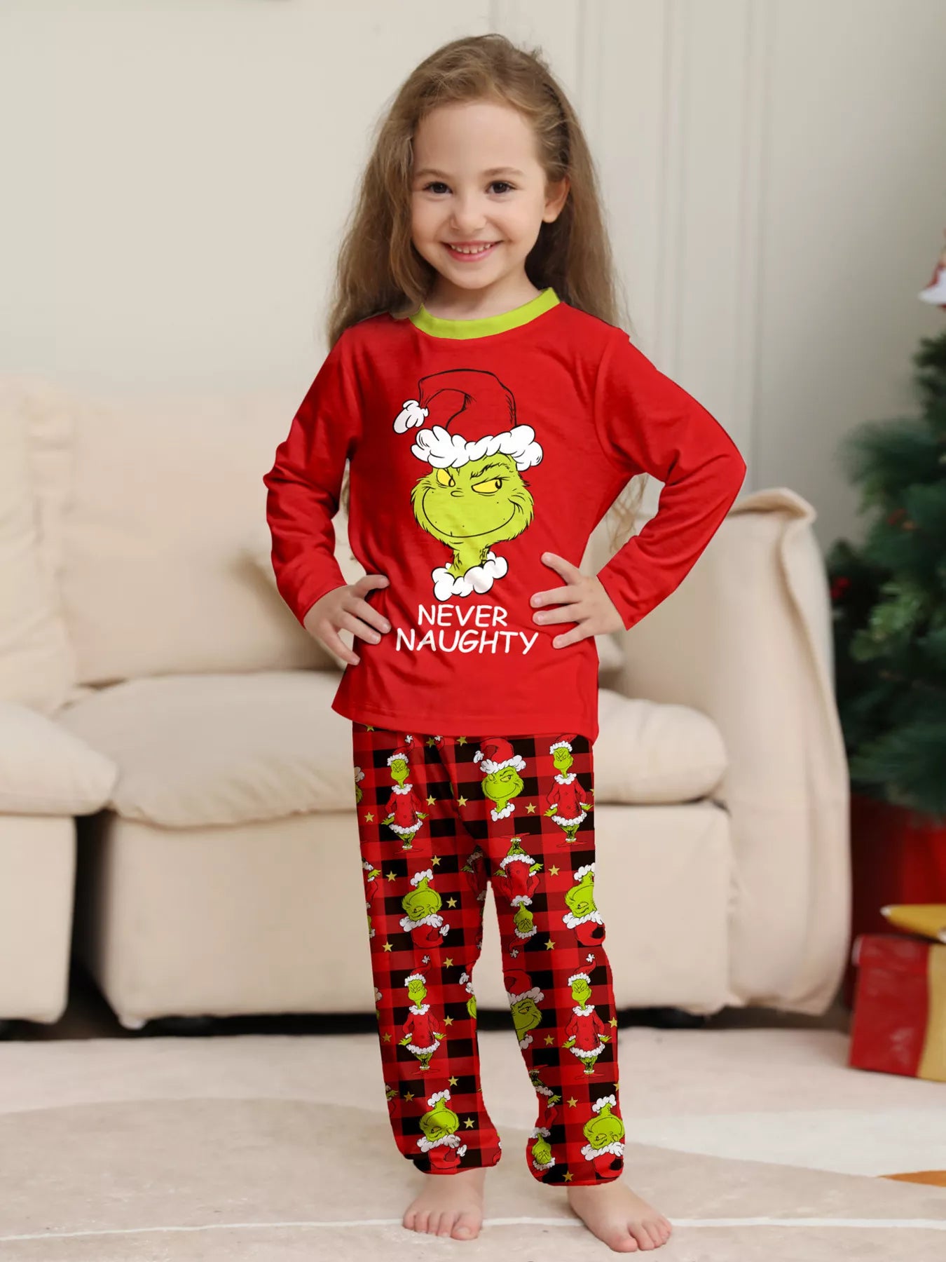 Girl wearing red Grinch-themed Christmas pajama sets with green character graphics and coordinating red plaid holiday pants.