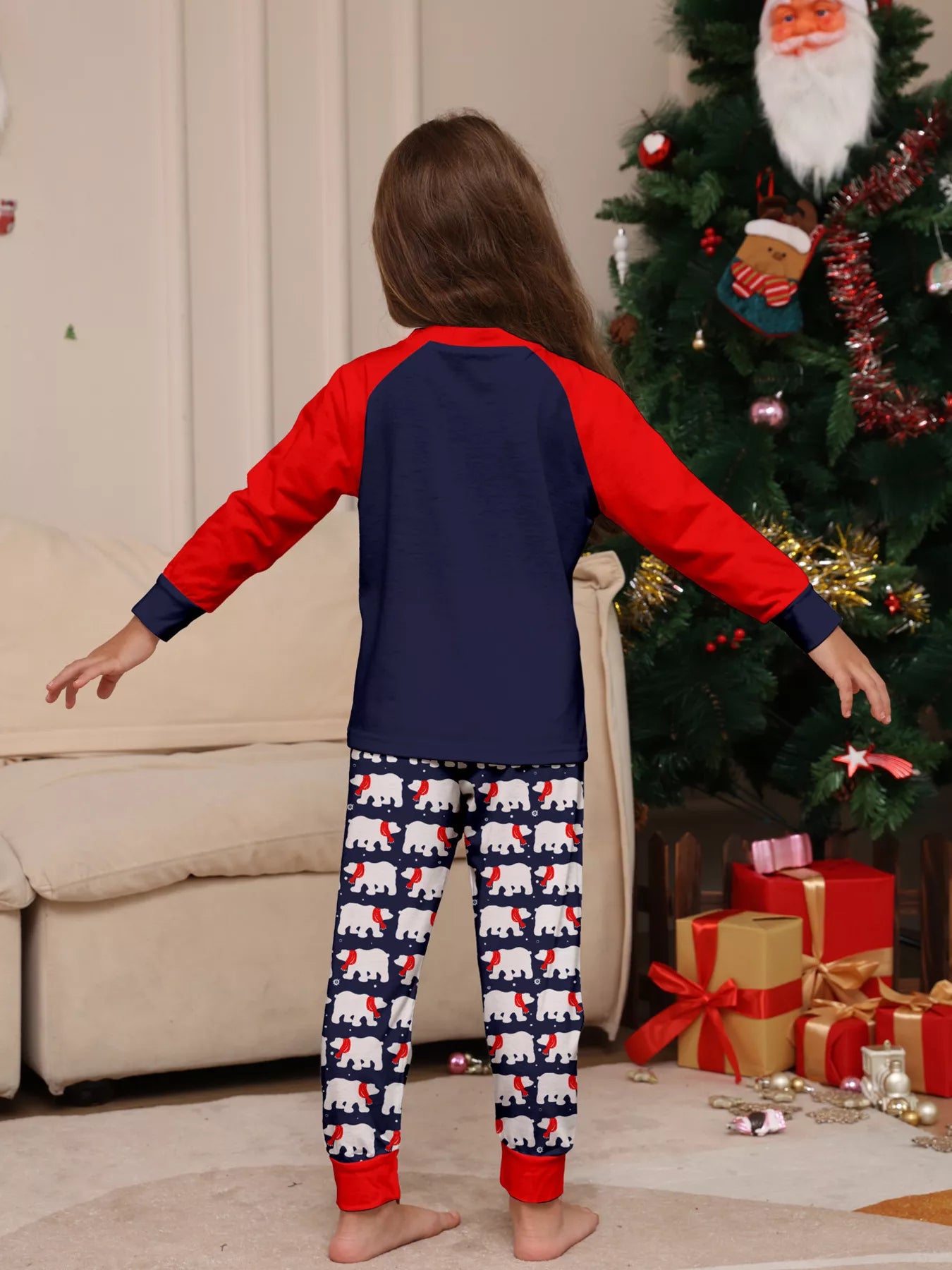 Girl wearing matching Christmas pajamas with navy tops, red raglan sleeves, festive Christmas tree lettering, and coordinating printed pants.
