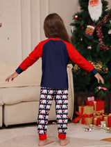 Girl wearing matching Christmas pajamas with navy tops, red raglan sleeves, festive Christmas tree lettering, and coordinating printed pants.