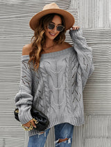 Woman wearing a gray cable knit openwork off-shoulder sweater with distressed jeans and a wide-brim hat.