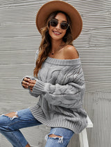 Woman wearing a gray cable knit openwork off-shoulder sweater with distressed jeans and a wide-brim hat.