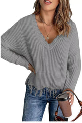 Woman wearing a gray ribbed V-neck sweater with distressed raw hem and blue jeans.