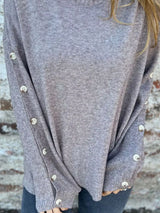 Woman wearing a gray ribbed turtleneck sweater with decorative button sleeves and jeans.