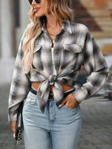 Woman wearing a gray plaid oversized button-up shirt layered over a white top with jeans and black crossbody bag.
