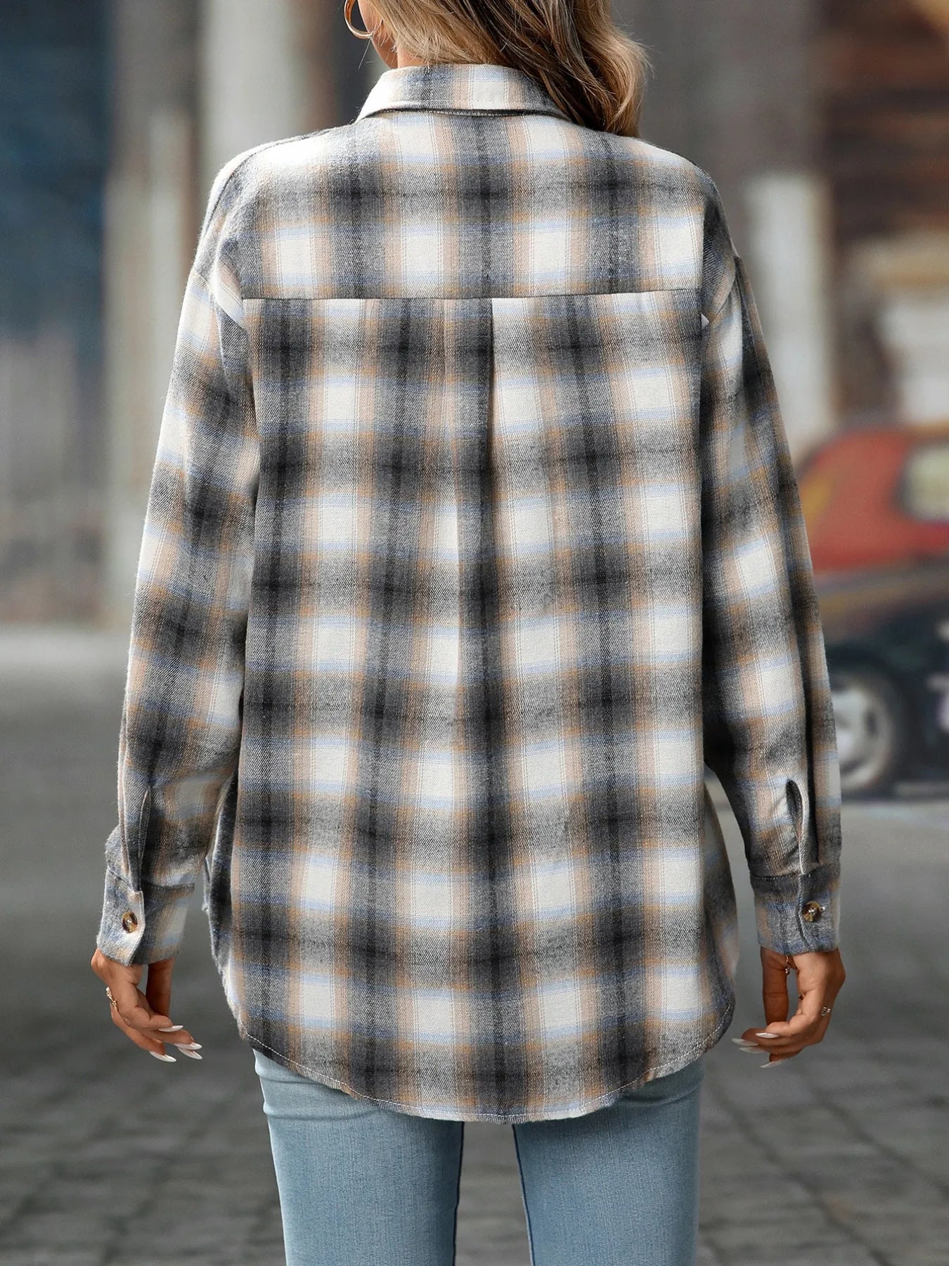 Woman wearing a gray plaid oversized button-up shirt layered over a white top with jeans.