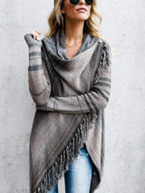 Woman wearing a gray stripe fringe long sleeve wrap cardigan with an asymmetrical draped front over a white top and jeans.