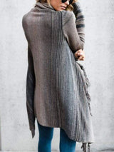 Woman wearing a gray stripe fringe long sleeve wrap cardigan with an asymmetrical draped front over a white top and jeans.