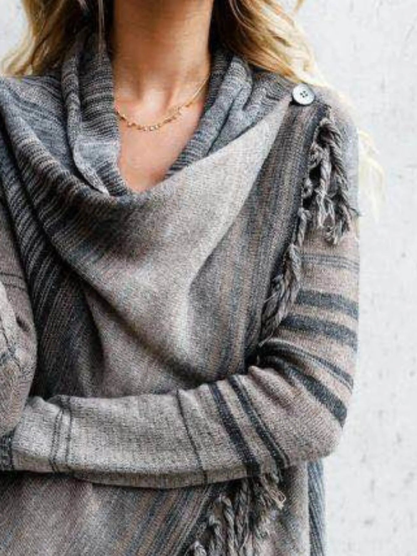 Woman wearing a gray stripe fringe long sleeve wrap cardigan with an asymmetrical draped front over a white top and jeans.