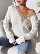 Woman wearing a gray/white V-neck hollow knit sweater with contrasting neckline, openwork long sleeves, and blue jeans.