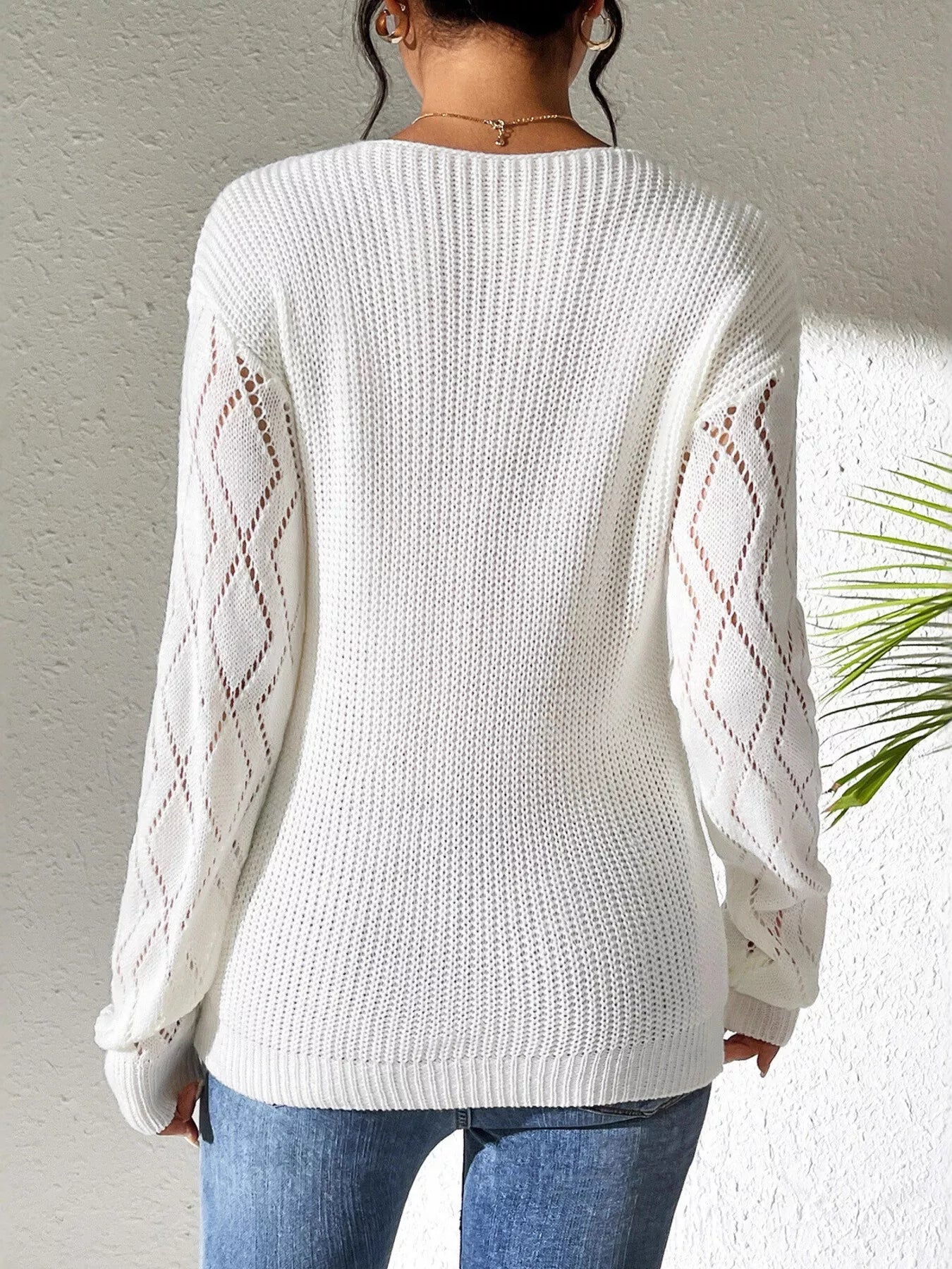 Woman wearing a gray/white V-neck hollow knit sweater with contrasting neckline, openwork long sleeves, and blue jeans.