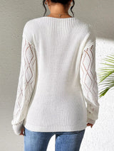 Woman wearing a gray/white V-neck hollow knit sweater with contrasting neckline, openwork long sleeves, and blue jeans.