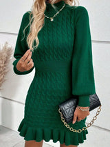 Woman wearing a green cable-knit sweater mini dress with mock neckline, long sleeves, fitted waist and feminine ruffled hem.