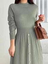 Woman wearing a green mock neck long sleeve knit midi dress with pleated skirt, front buttons and slit.