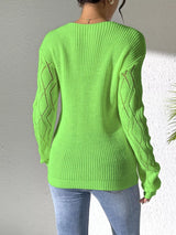 Woman wearing a green V-neck hollow knit sweater with contrasting neckline, openwork long sleeves, and blue jeans.