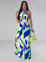 Woman wearing a colorful blue geometric patterned dress holding a green handbag on a gray background