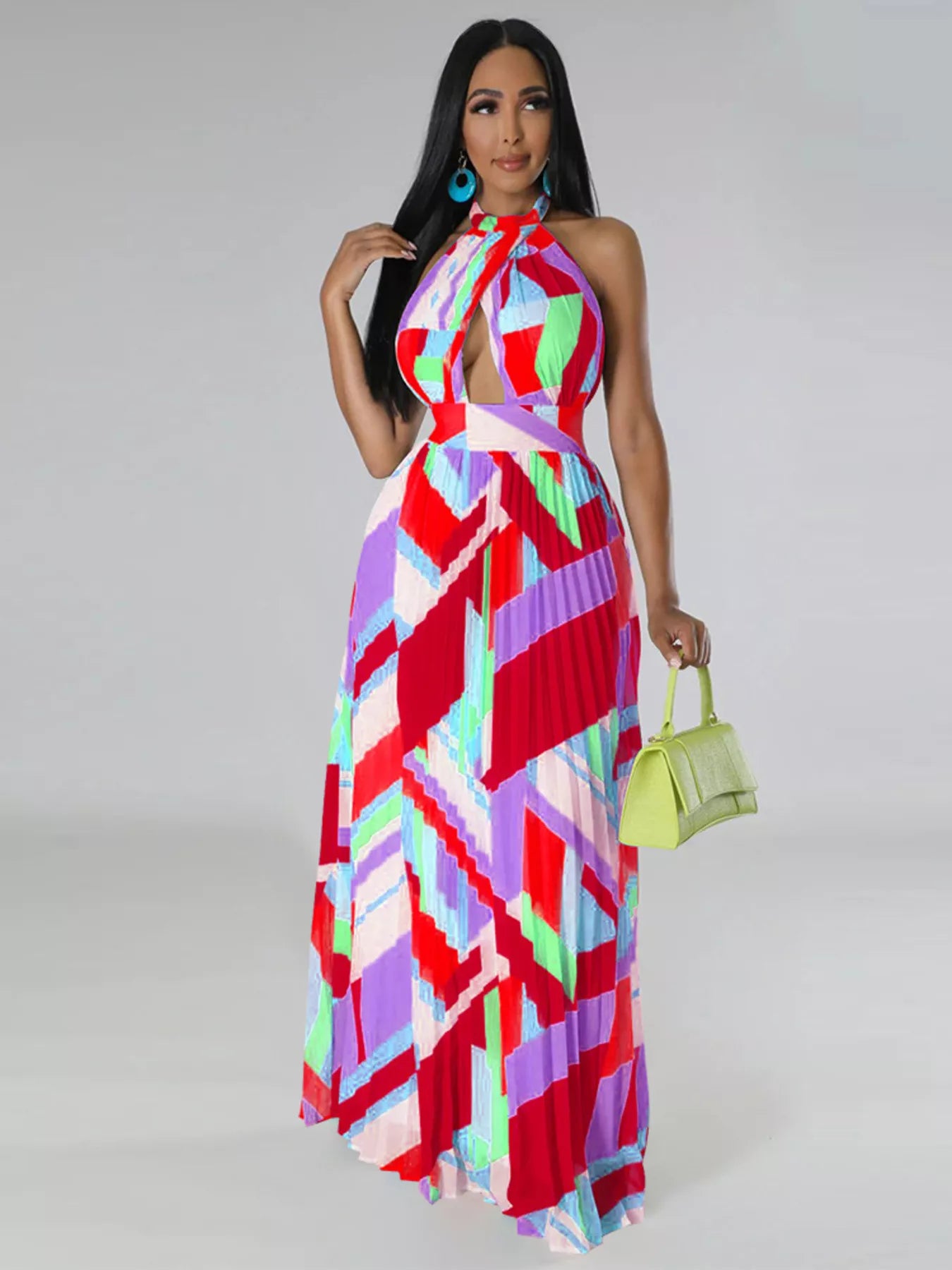 Woman wearing a colorful red geometric patterned dress holding a green handbag on a gray background