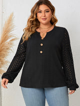 Woman wearing a black long-sleeve top with sheer sleeves against a white background