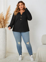 Woman wearing a black top with mesh sleeves and light blue jeans in a minimalistic room.