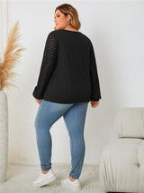 Woman wearing a black top with sheer sleeves and blue jeans in a minimalistic room showing the back of top.