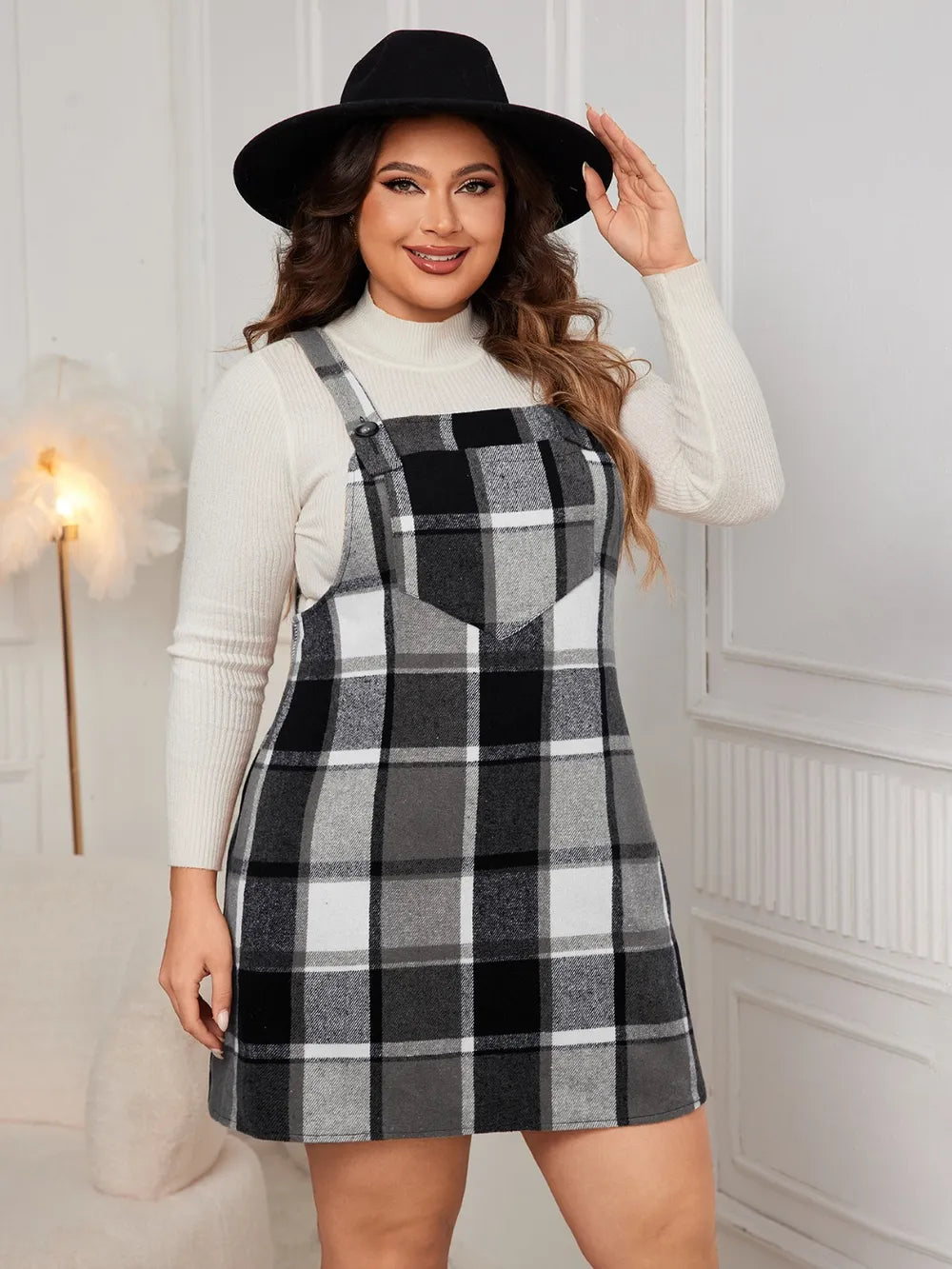 Woman wearing the Honey Plus Size Plaid Wide Strap Overall Dress layered over a cream mock neck sweater with a black felt hat, stylish plus size plaid fall dress from Chic Mystik Boutique.