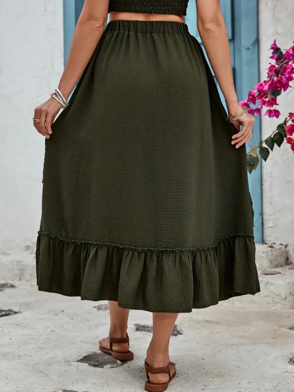 Back view of women's olive-green midi skirt with elastic waistband and wide ruffled hem.