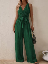 Woman wearing the Honey Tied Surplice Sleeveless Wide Leg Jumpsuit in dark green with a tie waist and wide-leg silhouette, elegant women's one-piece outfit from Chic Mystik Boutique.