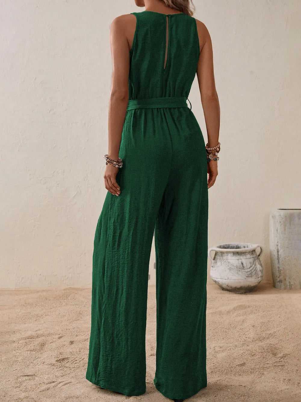 Woman wearing the Honey Tied Surplice Sleeveless Wide Leg Jumpsuit in dark green with a tie waist and wide-leg silhouette, elegant women's one-piece outfit from Chic Mystik Boutique.
