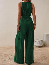 Woman wearing the Honey Tied Surplice Sleeveless Wide Leg Jumpsuit in dark green with a tie waist and wide-leg silhouette, elegant women's one-piece outfit from Chic Mystik Boutique.