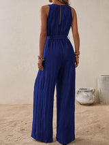 Woman wearing the Honey Tied Surplice Sleeveless Wide Leg Jumpsuit in indigo with a tie waist and wide-leg silhouette, elegant women's one-piece outfit from Chic Mystik Boutique.