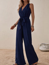 Woman wearing the Honey Tied Surplice Sleeveless Wide Leg Jumpsuit in navy with a tie waist and wide-leg silhouette, elegant women's one-piece outfit from Chic Mystik Boutique.
