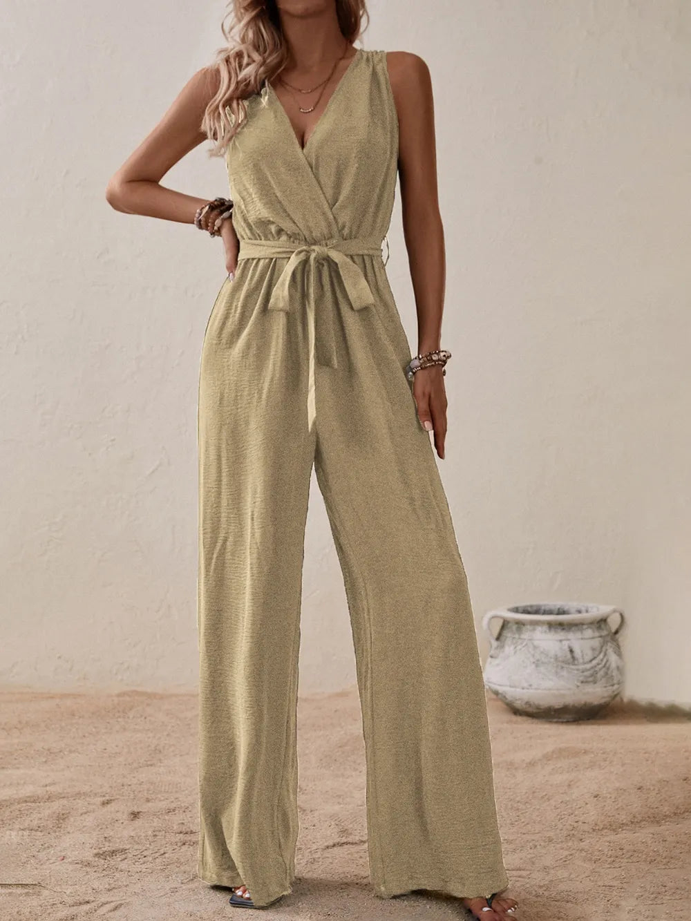 Woman wearing the Honey Tied Surplice Sleeveless Wide Leg Jumpsuit in tan with a tie waist and wide-leg silhouette, elegant women's one-piece outfit from Chic Mystik Boutique.