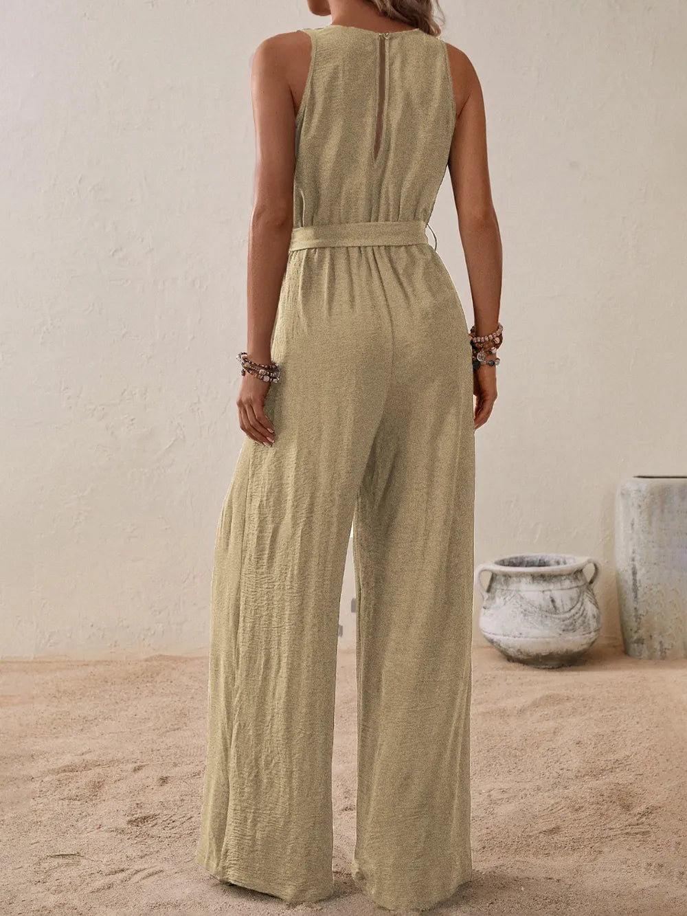 Woman wearing the Honey Tied Surplice Sleeveless Wide Leg Jumpsuit in tan with a tie waist and wide-leg silhouette, elegant women's one-piece outfit from Chic Mystik Boutique.
