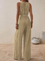 Woman wearing the Honey Tied Surplice Sleeveless Wide Leg Jumpsuit in tan with a tie waist and wide-leg silhouette, elegant women's one-piece outfit from Chic Mystik Boutique.