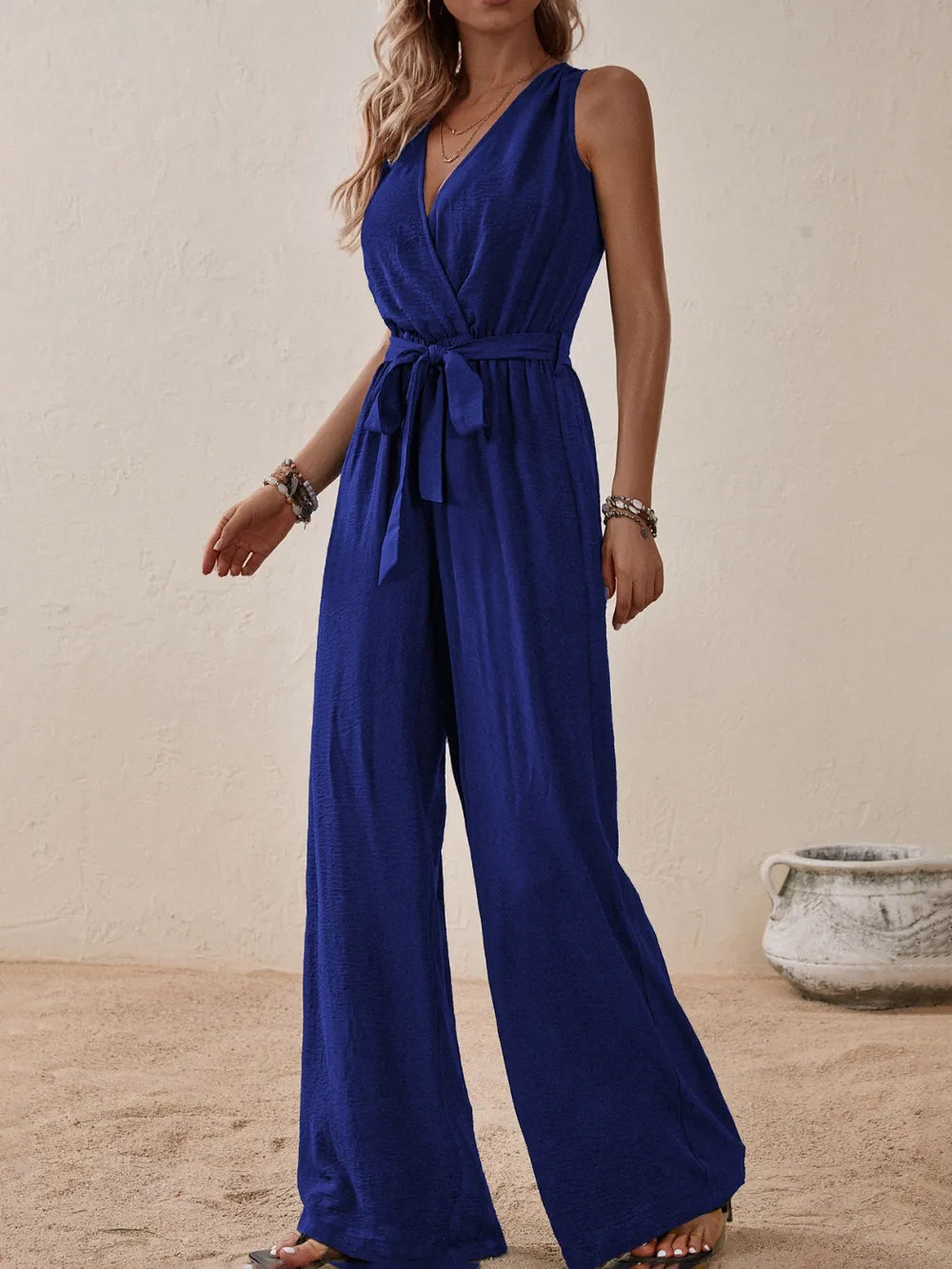 Woman wearing the Honey Tied Surplice Sleeveless Wide Leg Jumpsuit in indigo with a tie waist and wide-leg silhouette, elegant women's one-piece outfit from Chic Mystik Boutique.