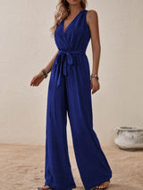 Woman wearing the Honey Tied Surplice Sleeveless Wide Leg Jumpsuit in indigo with a tie waist and wide-leg silhouette, elegant women's one-piece outfit from Chic Mystik Boutique.