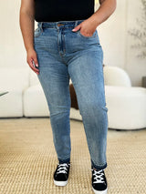 Judy Blue Full Size Mid Rise Rigid Magic Release Hem Jeans in medium wash featuring a flattering mid-rise fit, straight-leg silhouette, moderate stretch, and trendy raw release hem, styled with white sneakers.