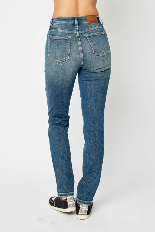 Model wearing Judy Blue high-waist skinny jeans in a medium wash with oversized front pockets and a slim, ankle-length fit, paired with black sneakers.