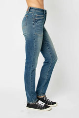 Model wearing Judy Blue high-waist skinny jeans in a medium wash with oversized front pockets and a slim, ankle-length fit, paired with black sneakers.