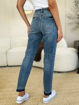 Judy Blue Full Size Mid Rise Rigid Magic Release Hem Jeans in medium wash featuring a flattering mid-rise fit, straight-leg silhouette, moderate stretch, and trendy raw release hem, styled with white sneakers.