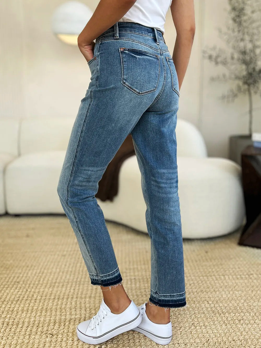 Judy Blue Full Size Mid Rise Rigid Magic Release Hem Jeans in medium wash featuring a flattering mid-rise fit, straight-leg silhouette, moderate stretch, and trendy raw release hem, styled with white sneakers.