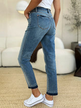 Judy Blue Full Size Mid Rise Rigid Magic Release Hem Jeans in medium wash featuring a flattering mid-rise fit, straight-leg silhouette, moderate stretch, and trendy raw release hem, styled with white sneakers.