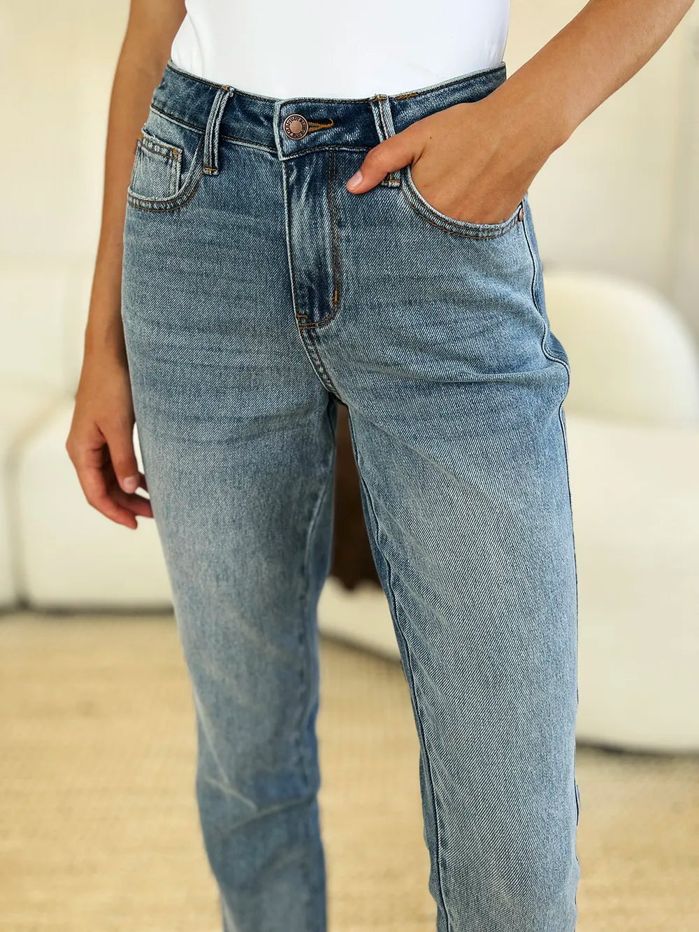 Judy Blue Full Size Mid Rise Rigid Magic Release Hem Jeans in medium wash featuring a flattering mid-rise fit, straight-leg silhouette, moderate stretch, and trendy raw release hem, styled with white sneakers.