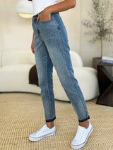 Judy Blue Full Size Mid Rise Rigid Magic Release Hem Jeans in medium wash featuring a flattering mid-rise fit, straight-leg silhouette, moderate stretch, and trendy raw release hem, styled with white sneakers.