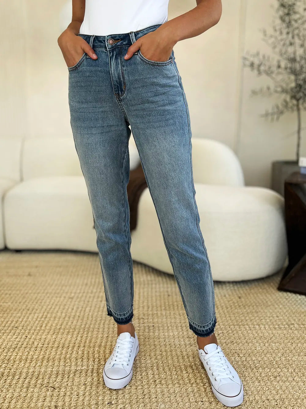 Judy Blue Full Size Mid Rise Rigid Magic Release Hem Jeans in medium wash featuring a flattering mid-rise fit, straight-leg silhouette, moderate stretch, and trendy raw release hem, styled with white sneakers.