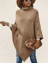 Back view of women's khaki knit turtleneck poncho pullover showing the loose draped silhouette and pointed hem, styled with blue jeans.