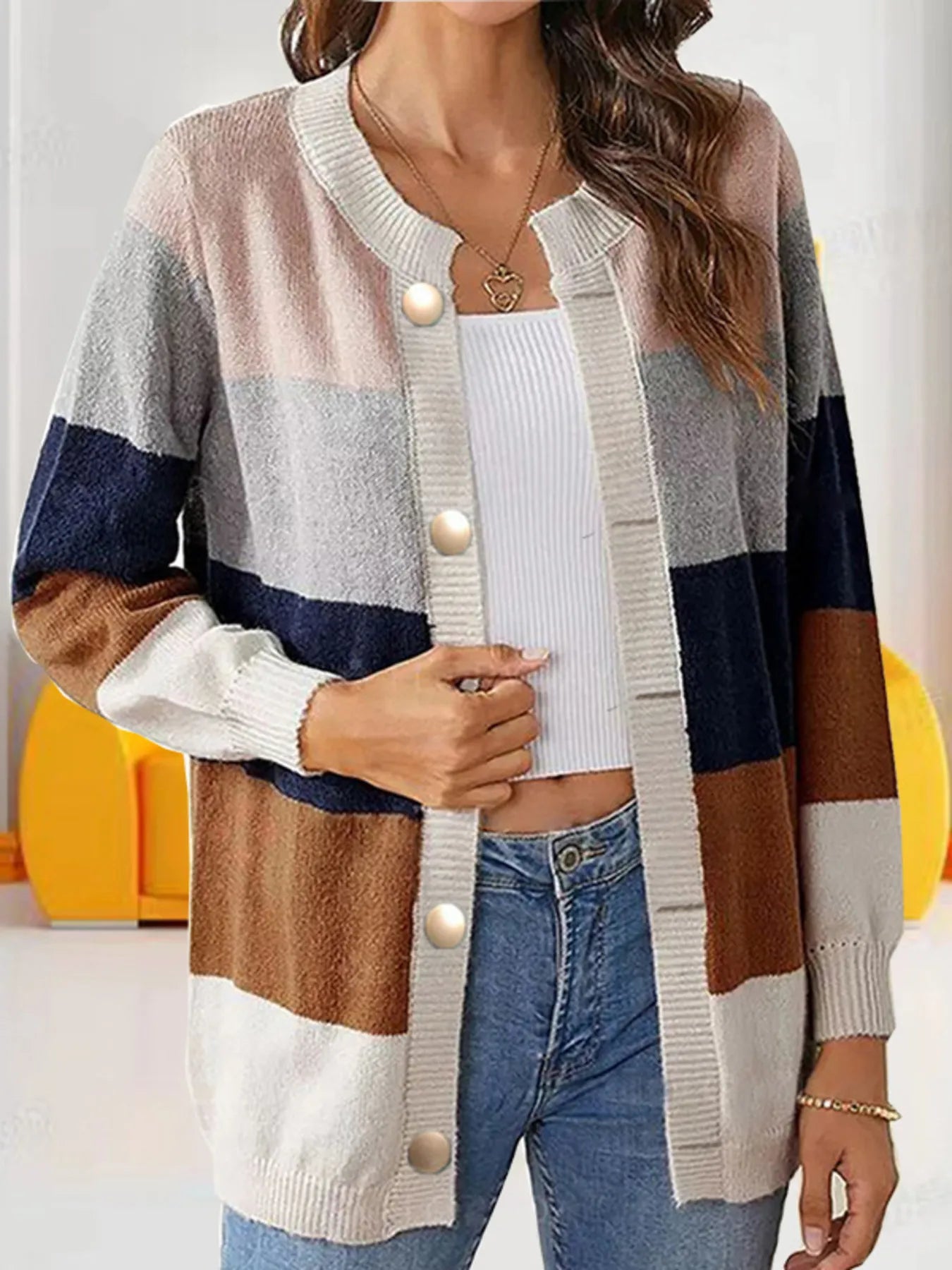 Women's khaki, light gray, and cream color block knit cardigan with round neckline, button-front closure, and ribbed trim, styled with a white top and blue jeans.