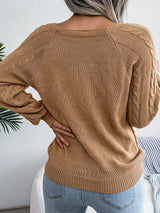Woman wearing an khaki cable-knit sweater with decorative buttons, paired with light-wash jeans, layered gold necklaces, and a white handbag. Perfect for cozy fall and winter outfits.