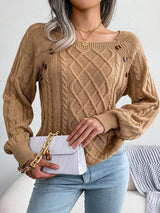 Woman wearing an khaki cable-knit sweater with decorative buttons, paired with light-wash jeans, layered gold necklaces, and a white handbag. Perfect for cozy fall and winter outfits.