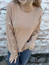 Woman wearing a khaki ribbed turtleneck sweater with decorative button sleeves and jeans.